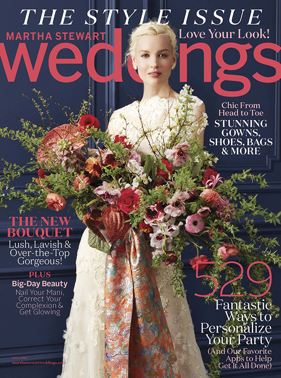 Martha Steward Wedding cover featuring a Bride with a fair complexion, blonde updo, and white floral dress holding a large bouquet. The bouquet has long greenery reach out, with a mix of different red, pink, and orange color flowers throughout. The bouquet is tied together with an orange silk ribbon with multicolor flowers. The issue is titled "The Style Issue, Love your Look" from Fall, 2016.