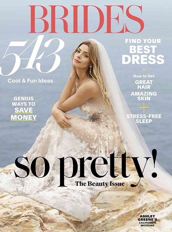 Brides Magazine cover, issue number 543, featuring a bride kneeling on a rock pint in front of pale blue water in a sleeveless floral lace gown and tulle veil. Large black text reads "So pretty! The beauty issue."